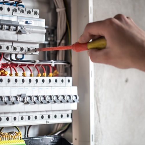 man-electrical-technician-working-switchboard-with-fuses-installation-connection-electrical-equipment-close-up